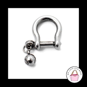 May include: A silver metal key chain with a round charm. The charm has a textured surface and a small loop at the top.