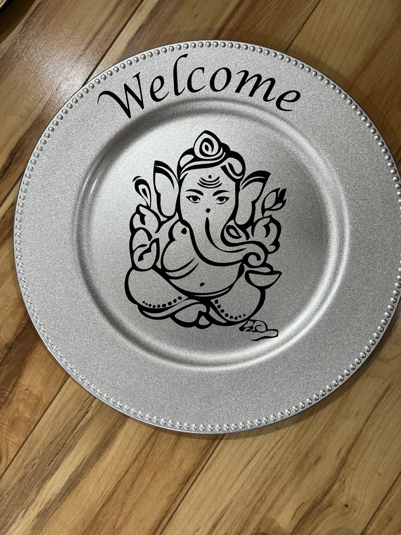 May include: Silver charger plate with a black and white image of Ganesha and the word "Welcome" in black lettering.