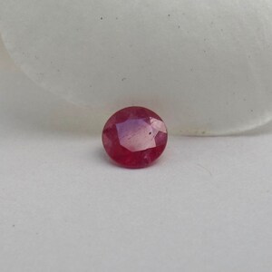 Puede incluir: Una piedra preciosa de rubí redonda y facetada de color rojo intenso.