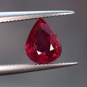May include: A deep red pear-shaped gemstone held by tweezers.