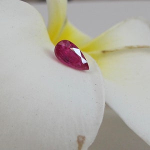 May include: A pear-shaped ruby gemstone with a deep red colour. The gemstone is set against a white background.