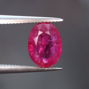 Pode incluir: Uma gema de rubi ovalada de cor rosa vibrante, segurada em uma pinça.