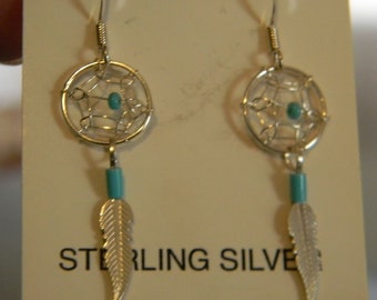 May include: Sterling silver dreamcatcher earrings. Each earring features a circular web design with a turquoise bead in the center, a turquoise bead below, and a silver feather charm. The earrings hang from a silver hook.