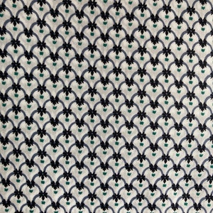 May include: A close-up of a fabric with a repeating pattern. The design features a series of interconnected, stylized floral motifs in black, blue-grey, and green against a cream-coloured background. The pattern creates a textured, visually appealing surface.