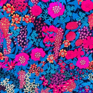 Op de afbeelding: Een levendige bloemenprintstof met een verscheidenheid aan roze, oranje, blauwe en paarse bloemen op een zwarte achtergrond.