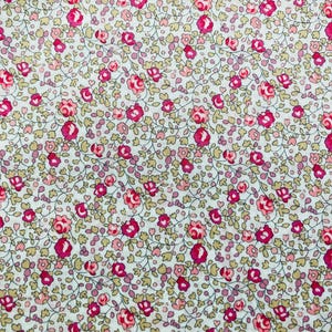 May include: A white fabric with a repeating pattern of small pink and red flowers and green leaves.