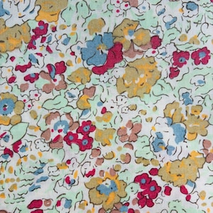 May include: A white fabric featuring a dense, repeating floral pattern. The design consists of small, stylised flowers in shades of mustard yellow, bright magenta, sky blue, and soft brown, interspersed with light mint green foliage and stems.