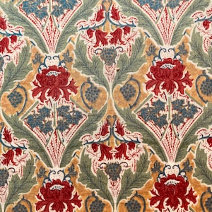 May include: A repeating pattern of red, green and blue floral motifs on a beige background. The design features stylised flowers, leaves and vines.