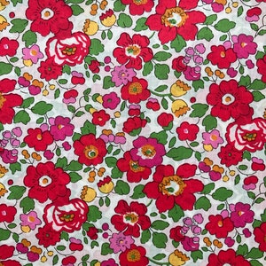 以下が含まれることがあります： 赤とピンクの花柄の白い生地。花は小さく密集しており、賑やかで鮮やかなデザインになっています。