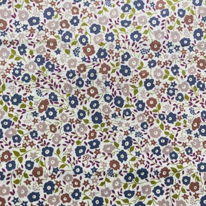May include: A white fabric with a repeating pattern of small blue, purple, and brown flowers. The flowers are scattered randomly across the fabric.