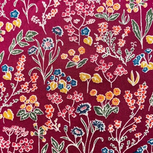 May include: A burgundy fabric with a repeating pattern of small white, yellow, blue, and red flowers. The flowers are arranged in a random pattern on the fabric.
