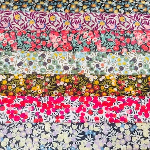 Puede incluir: Una selección de muestras de tela floral colorida. Las telas presentan varios patrones de flores y hojas en tonos de rojo, rosa, azul, amarillo y verde. Las palabras "LIBERTY FABRICS" están impresas en un letrero de madera.