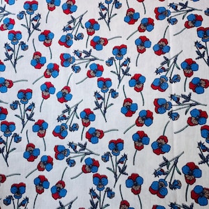 Op de afbeelding: Witte stof met een herhalend patroon van blauwe en rode viooltjes en groene stelen. De bloemen zijn verspreid over de stof, waardoor een bloemenontwerp ontstaat. De stof lijkt katoen of een vergelijkbaar materiaal te zijn.