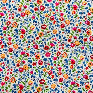 Puede incluir: Una tela blanca con un patrón repetitivo de pequeñas flores azules, rojas, amarillas y rosas. Las flores están dispuestas en un patrón aleatorio en la tela.