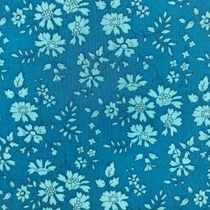 May include: Close-up of a teal fabric with a floral pattern. The design features light blue flowers and leaves scattered across the teal background. The flowers vary in size and are clustered together, creating a delicate and intricate design. This fabric is suitable for various sewing projects.