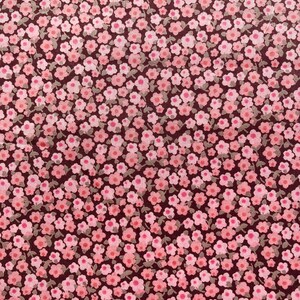 Può includere: Un tessuto marrone scuro con un motivo ripetitivo di piccoli fiori rosa. I fiori sono sparsi casualmente sul tessuto.