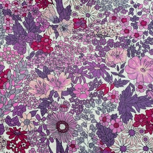 May include: A close-up of a floral fabric with a dense pattern of various flowers in shades of purple, pink, and white. The flowers include daisies, dahlias, and other blooms, with green leaves. The fabric has a vintage or cottagecore aesthetic.