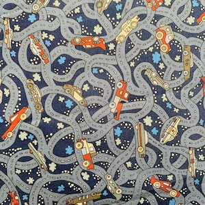 May include: A blue fabric with a repeating pattern of cars and roads. The cars are red, yellow, and green. The roads are grey and winding. There are small white flowers scattered throughout the pattern.