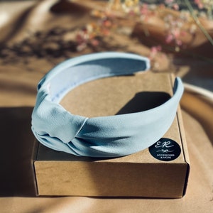 Peut inclure: Un serre-tête noué bleu clair sur une boîte brune avec un autocollant noir qui dit "E&R by Accessories & More".