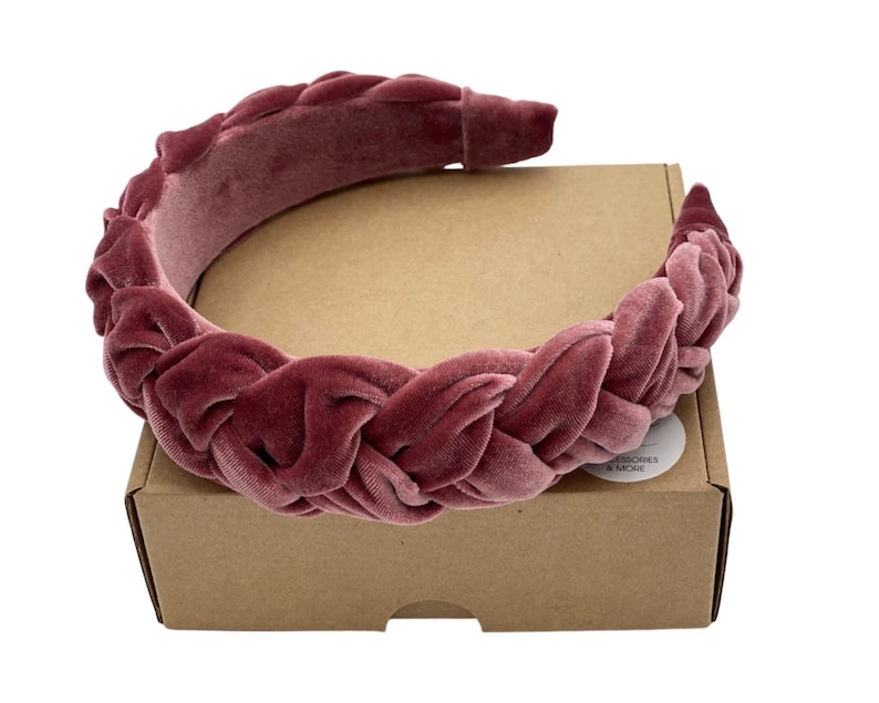 Peut inclure: Un serre-t&ecirc;te en velours rose avec un design tress&eacute;. Le serre-t&ecirc;te est sur une bo&icirc;te brune avec le texte "ACCESSORIES & MORE" sur un autocollant blanc.