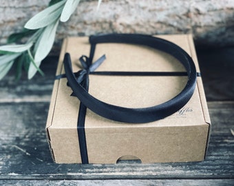 May include: A black satin headband in a brown cardboard box with a black ribbon tied around it. The box has the text "Ruffles" printed on it.