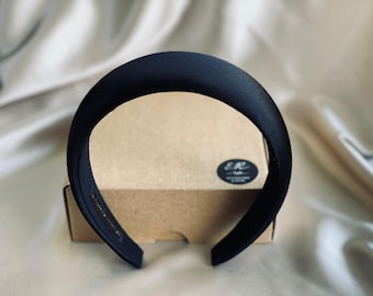 May include: A black satin headband with a wide, curved design. The headband is sitting on a brown box with a white label that says "E&R".