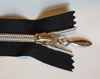 May include: A black zipper with a silver slider and pull tab. The zipper is open and the teeth are visible.