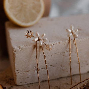 Puede incluir: Dos horquillas doradas con detalles de flores de perlas. Las horquillas son onduladas y tienen un dise&ntilde;o delicado.