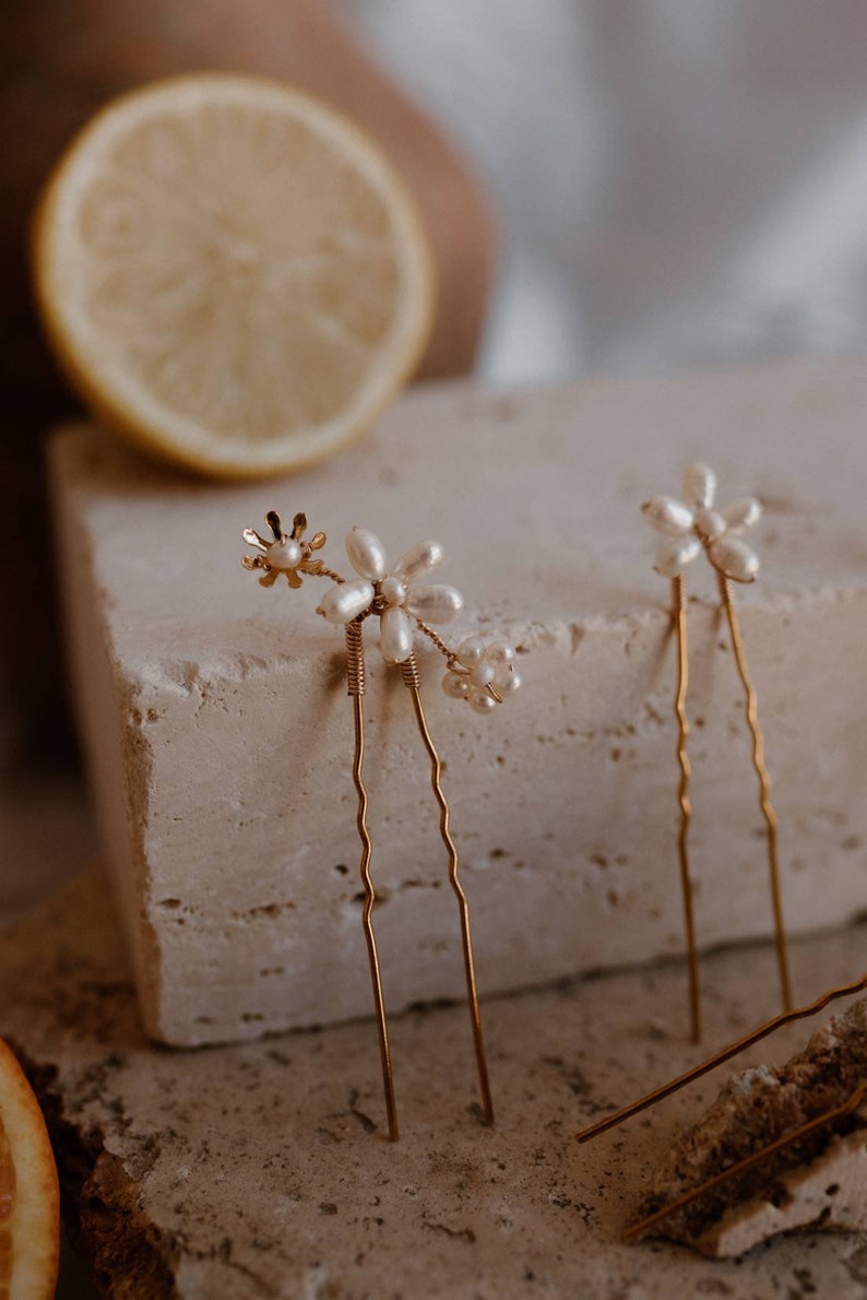 Puede incluir: Dos horquillas doradas con detalles de flores de perlas. Las horquillas son onduladas y tienen un dise&ntilde;o delicado.