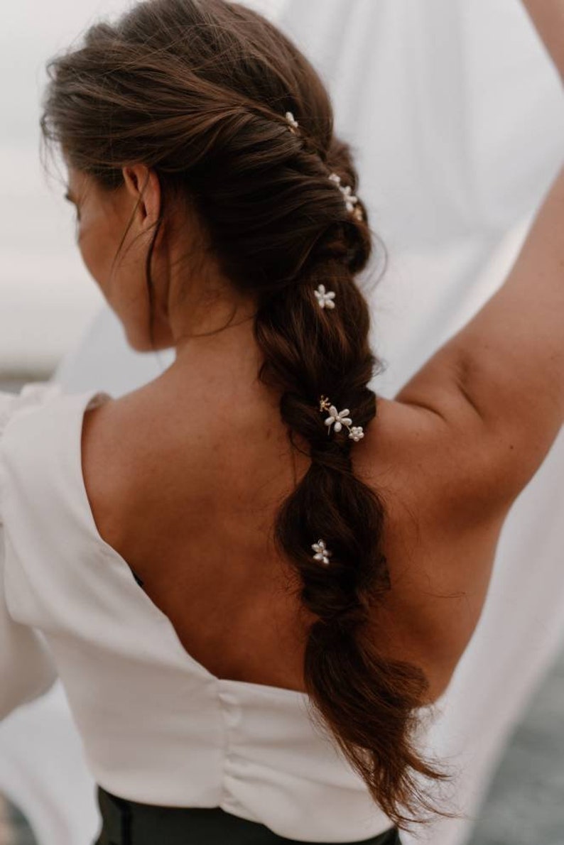 Puede incluir: Una mujer con el pelo largo y casta&ntilde;o peinado en una trenza con peque&ntilde;as pinzas para el pelo con forma de flores blancas. Las pinzas para el pelo est&aacute;n dispersas por toda la trenza.