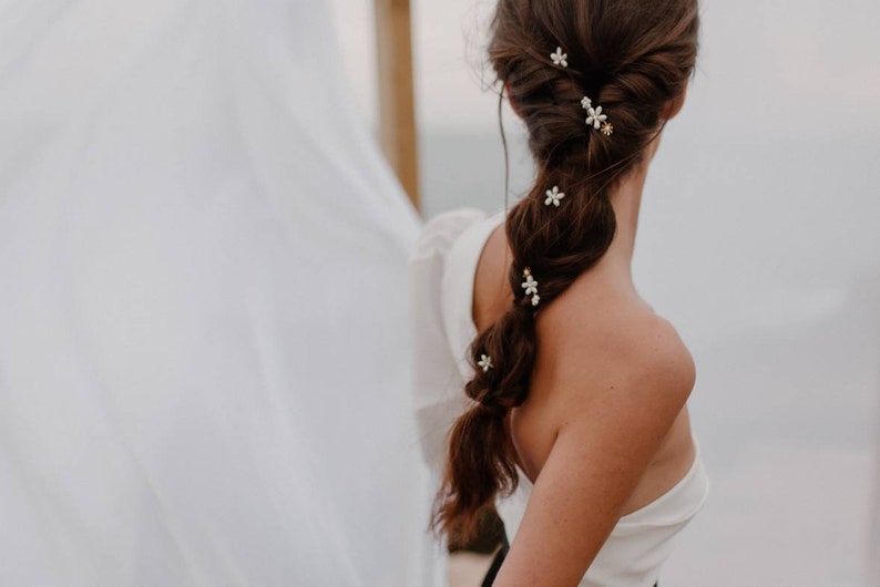 Puede incluir: Una mujer con el pelo largo y casta&ntilde;o peinado en una trenza con peque&ntilde;as pinzas para el pelo con forma de flores blancas. Las pinzas para el pelo est&aacute;n dispersas por toda la trenza.
