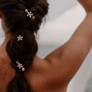 Puede incluir: Una mujer con el pelo largo y casta&ntilde;o peinado en una trenza con cinco peque&ntilde;as pinzas para el pelo con forma de flor blanca. Las pinces para el pelo tienen detalles dorados.