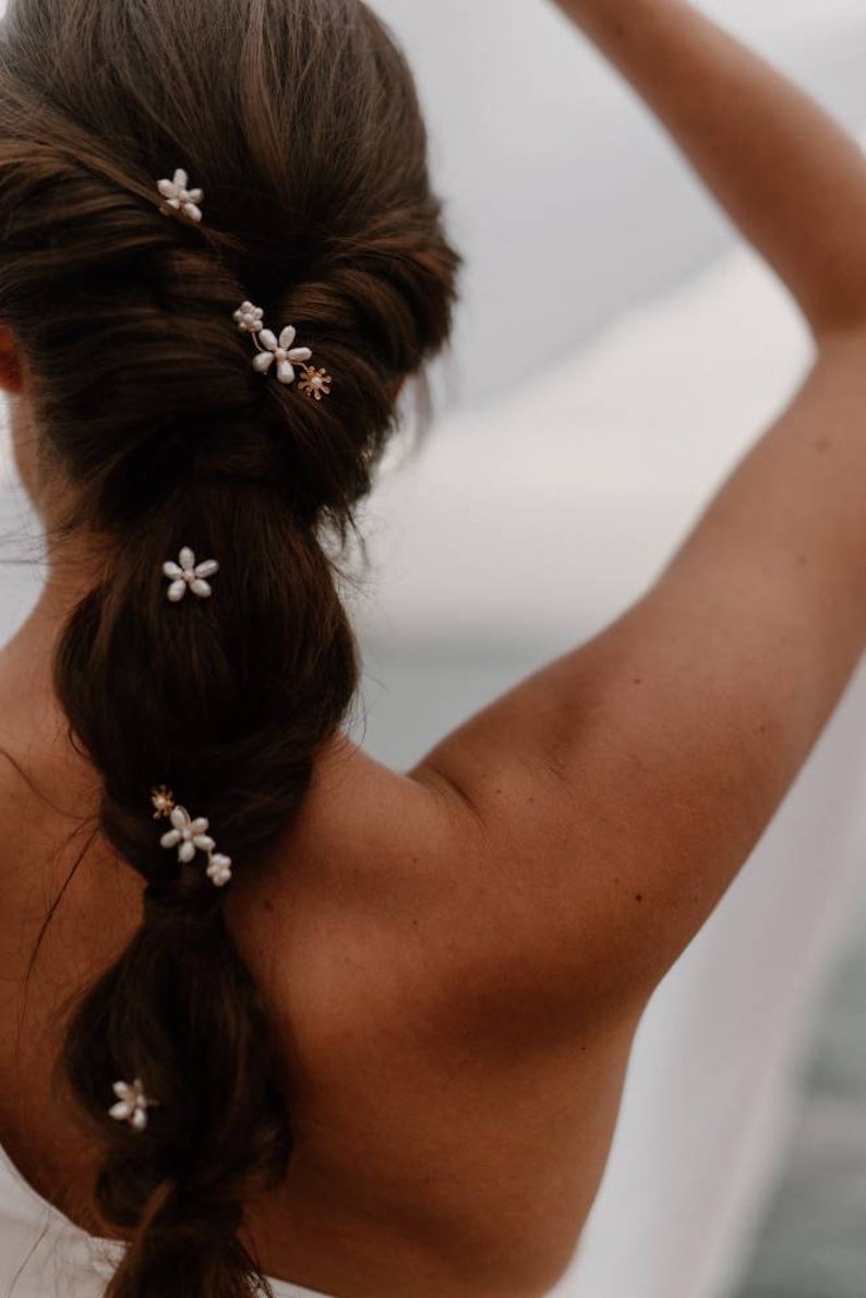 Puede incluir: Una mujer con el pelo largo y casta&ntilde;o peinado en una trenza con cinco peque&ntilde;as pinzas para el pelo con forma de flor blanca. Las pinces para el pelo tienen detalles dorados.