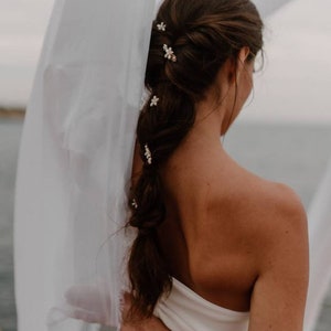 Puede incluir: Una mujer con el pelo largo y casta&ntilde;o peinado en una trenza con peque&ntilde;as pinzas para el pelo con forma de flores blancas. Lleva un top blanco sin tirantes y una falda negra.