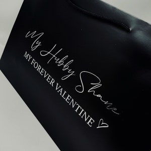 May include: Black gift bag with a white inscription that reads "My Hubby Shane" and "My Forever Valentine" with a heart symbol.