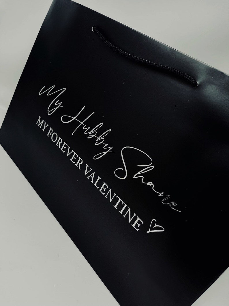 May include: Black gift bag with a white inscription that reads "My Hubby Shane" and "My Forever Valentine" with a heart symbol.