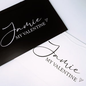 May include: Two gift bags, one black and one white, with the text "Jamie My Valentine" in white lettering on the black bag and black lettering on the white bag.