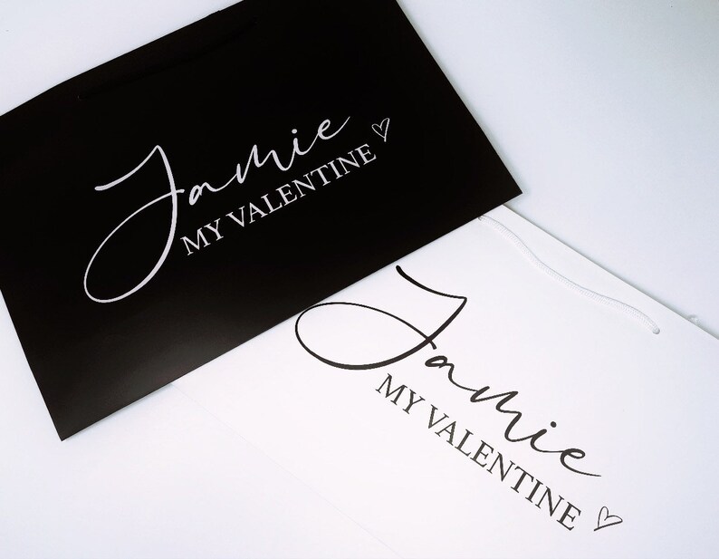 May include: Two gift bags, one black and one white, with the text "Jamie My Valentine" in white lettering on the black bag and black lettering on the white bag.
