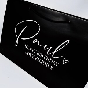 May include: Black gift bag with white text that says "Paul Happy Birthday Love Eilidh X" and a heart.