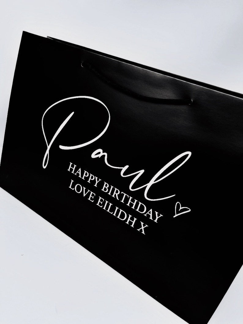 May include: Black gift bag with white text that says "Paul Happy Birthday Love Eilidh X" and a heart.
