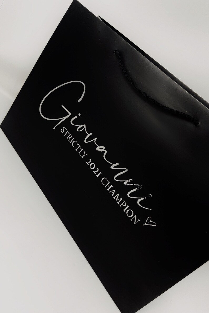 May include: Black shopping bag with a white logo that says "Giovanni" and "Strictly 2021 Champion" with a heart.