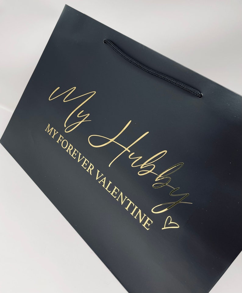 May include: Black gift bag with a gold inscription that reads "My Hubby My Forever Valentine" with a heart symbol.