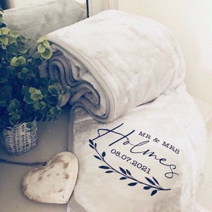Puede incluir: Una manta suave y gris con un mensaje personalizado que dice "MR & MRS Holmes 08.07.2021" con un diseño floral.