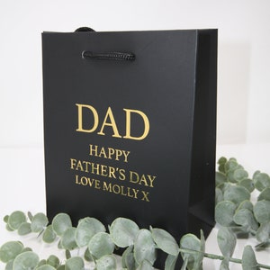 Puede incluir: Bolsa de regalo negra con una inscripción dorada que dice "DAD Happy Father's Day Love Molly X".