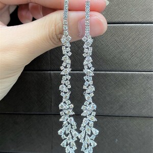 May include: A pair of long, silver dangle earrings with a cascading design of small, clear cubic zirconia stones.