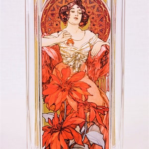 Könnte beinhalten: Eine klare Glasvase mit rechteckiger Form und einem dekorativen Bild einer Frau in einem roten Kleid mit roten Blumen. Das Bild ist von einem goldenen Rahmen mit einem geometrischen Muster umgeben.