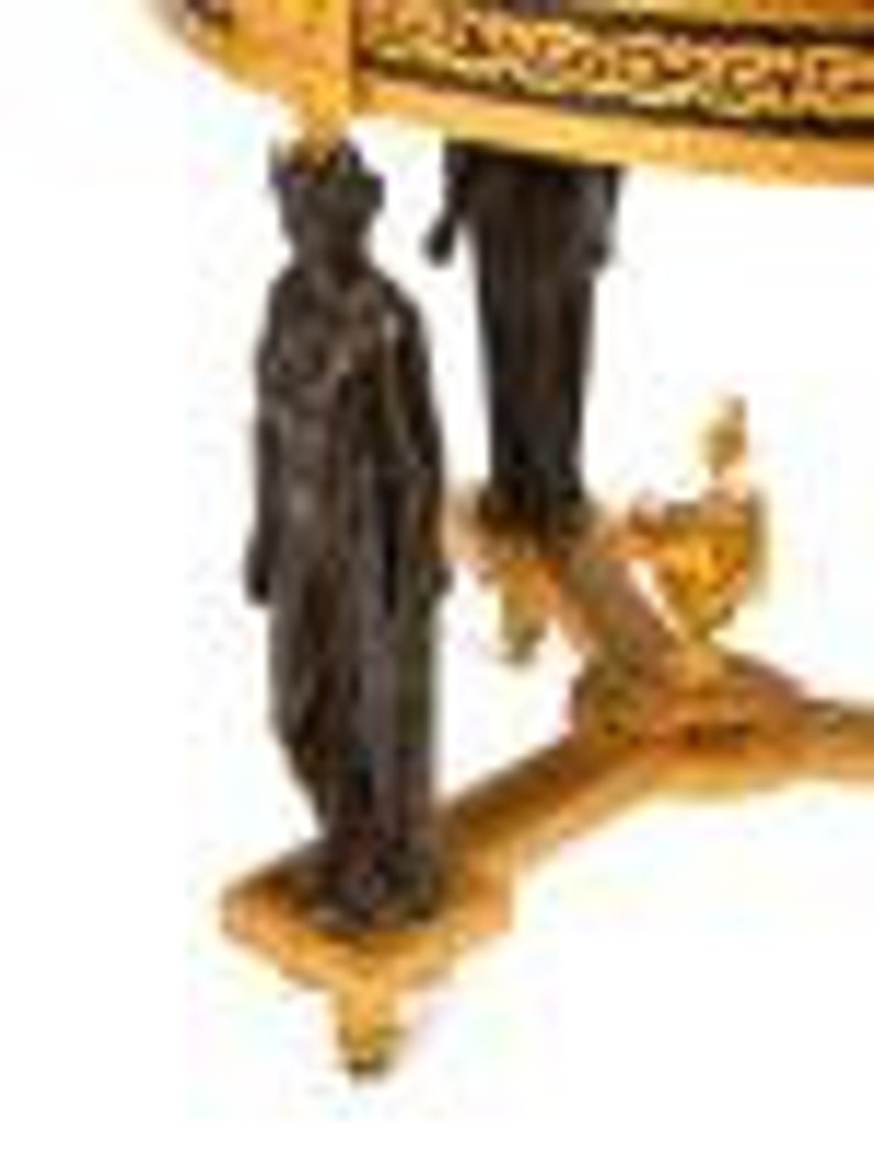 May include: A round, wooden table with a gold and black patterned top. The table has a decorative base with a bronze figure on each side.
