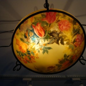 Może przedstawiać: Okrągły, żółtawy klosz lampy z czarną metalową ramą. Klosz zdobi kwiatowy wzór z różowymi, czerwonymi i żółtymi kwiatami oraz zielonymi liśćmi.