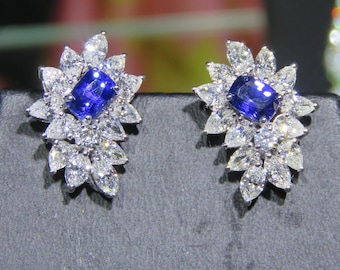 May include: A pair of silver earrings with a blue sapphire gemstone surrounded by a cluster of smaller diamonds.