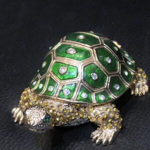 Pode incluir: Uma figura de tartaruga verde e dourada adornada com joias, com uma casca detalhada e detalhes brilhantes.